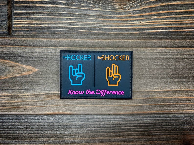 K&ouml;nnte beinhalten: Schwarzer Patch mit wei&szlig;en N&auml;hten, der zwei Handgesten zeigt, eine in Blau und eine in Orange, mit dem Text "the ROCKER" und "the SHOCKER" &uuml;ber jeder Hand. Der Text "Know the Difference" ist in Pink unter den H&auml;nden geschrieben.