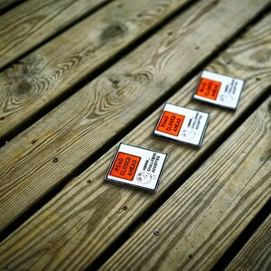 Op de afbeelding: Drie oranje en zwarte borden met de tekst 'Weg afgesloten' met een cartoonfiguur dat de uitdaging aanneemt. De borden liggen op een houten oppervlak.