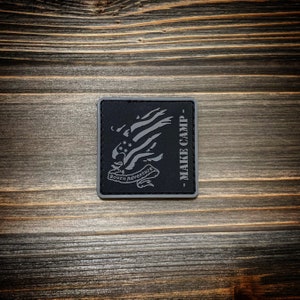 Peut inclure: Un patch brodé noir et gris avec un aigle et un motif de drapeau américain. Le patch porte le texte "Bourn Adventure" et "MAKE CAMP".