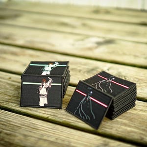 May include: Two stacks of black fabric patches with images of Star Wars characters. One stack features Luke Skywalker and the other Darth Vader.
