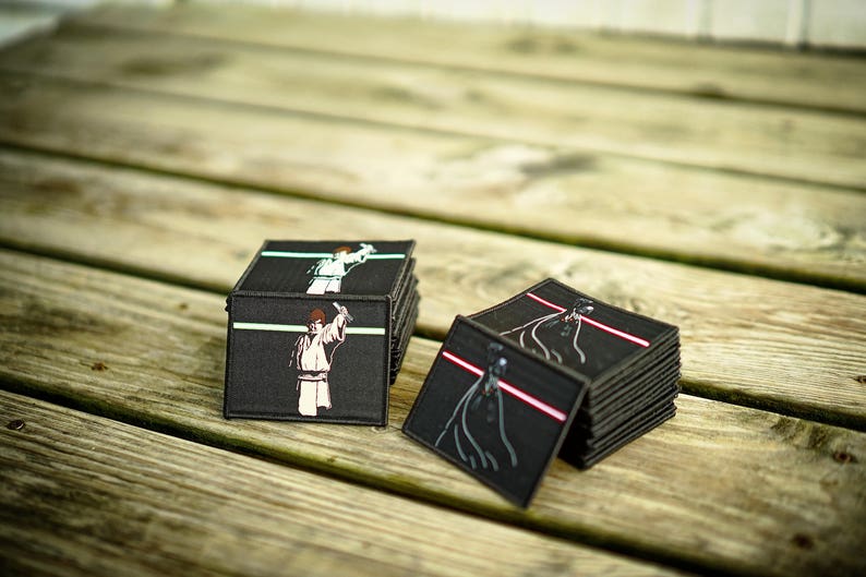 May include: Two stacks of black fabric patches with images of Star Wars characters. One stack features Luke Skywalker and the other Darth Vader.
