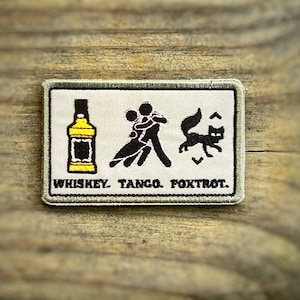 Può includere: Un cerotto in tessuto beige con sfondo bianco e testo e immagini nere. Il cerotto presenta una bottiglia di whisky, una coppia che balla e una volpe. Il testo recita "Whiskey Tango Foxtrot."