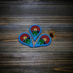 May include: Three blue, red, and brown felt patches shaped like teardrops with a mountain scene and a sun inside each patch.