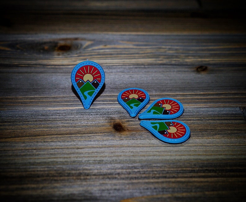 May include: Four blue and red pinback buttons with a mountain and sun design. The buttons are arranged in a circle on a wooden surface.