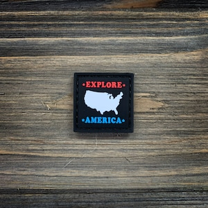 Può includere: Toppa nera con un contorno bianco degli Stati Uniti e il testo "*EXPLORE* AMERICA*" in rosso e blu.