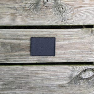 May include: A black fabric patch with a rough texture, placed on a wooden surface.