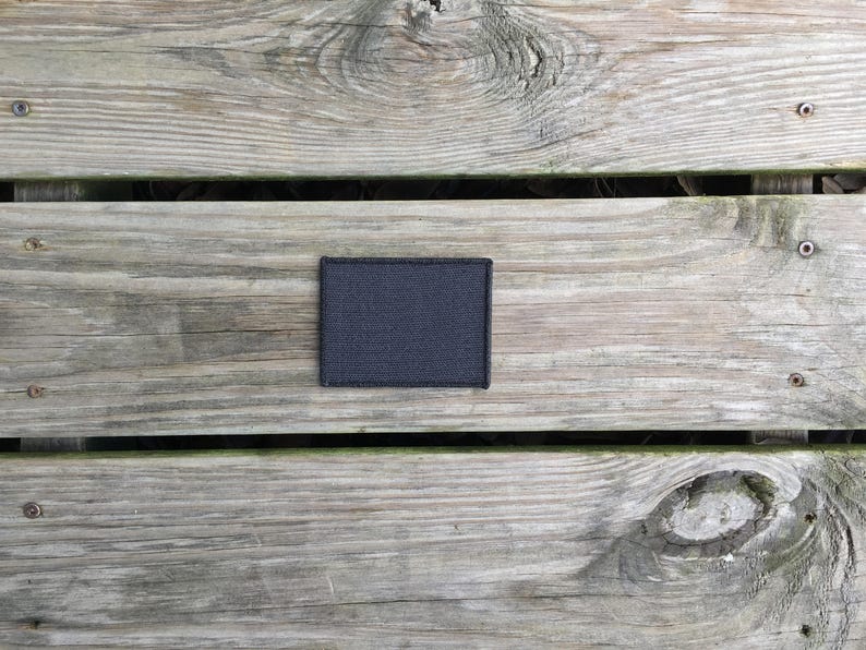 May include: A black fabric patch with a rough texture, placed on a wooden surface.