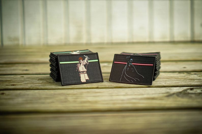 May include: Two black fabric patches with embroidered images of Star Wars characters. The left patch shows Luke Skywalker holding a lightsaber with a green blade. The right patch shows Darth Vader holding a lightsaber with a red blade.