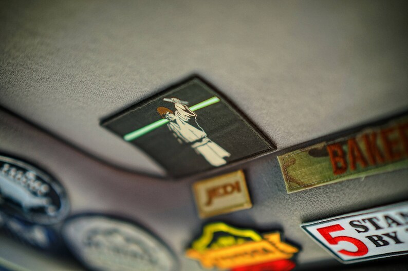 May include: A collection of colourful patches, including a Star Wars themed patch with a character wielding a lightsaber, a patch with the word "BAKER" in white letters on a green background, and a patch with the text "STAND BY" and the number "5" in white on a red background.