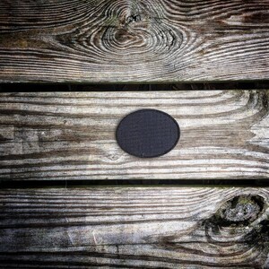May include: A close-up of a black circle patch on a weathered wooden surface. The wood has a natural grain pattern and appears to be made of planks.