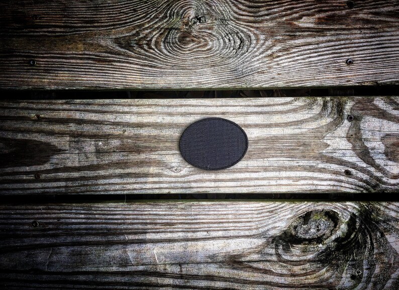 May include: A close-up of a black circle patch on a weathered wooden surface. The wood has a natural grain pattern and appears to be made of planks.