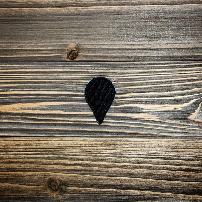 May include: A black fabric patch in the shape of a teardrop with a pointed tip. The patch is on a wooden surface.