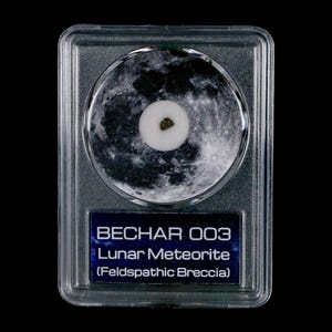 Op de afbeelding: Een maanmeteorietmonster, gelabeld "Bechar 003", in een heldere beschermende houder. Het monster is geplaatst tegen een achtergrond die het oppervlak van de maan afbeeldt. Het label geeft ook aan dat de meteoriet Feldspathic Breccia is.