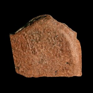 Peut inclure: Un gros plan d'un tesson de poterie brun rougeâtre avec une surface rugueuse et texturée. Le tesson est de forme irrégulière et a un bord légèrement incurvé.