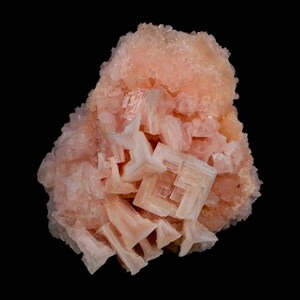 May include: A cluster of pale pink, translucent mineral crystals featuring geometric, stepped, and layered formations. The specimen displays a variety of sharp, angular edges and crystalline structures with a soft, light peach-coloured hue throughout.