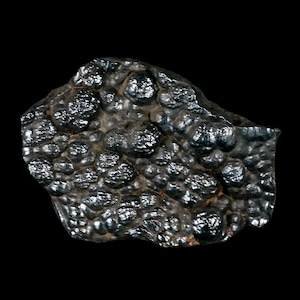May include: A dark, metallic-looking mineral specimen with a bumpy, rounded surface. The color is a deep, reflective black with hints of silver. The texture appears rough and uneven, with many small, spherical formations.