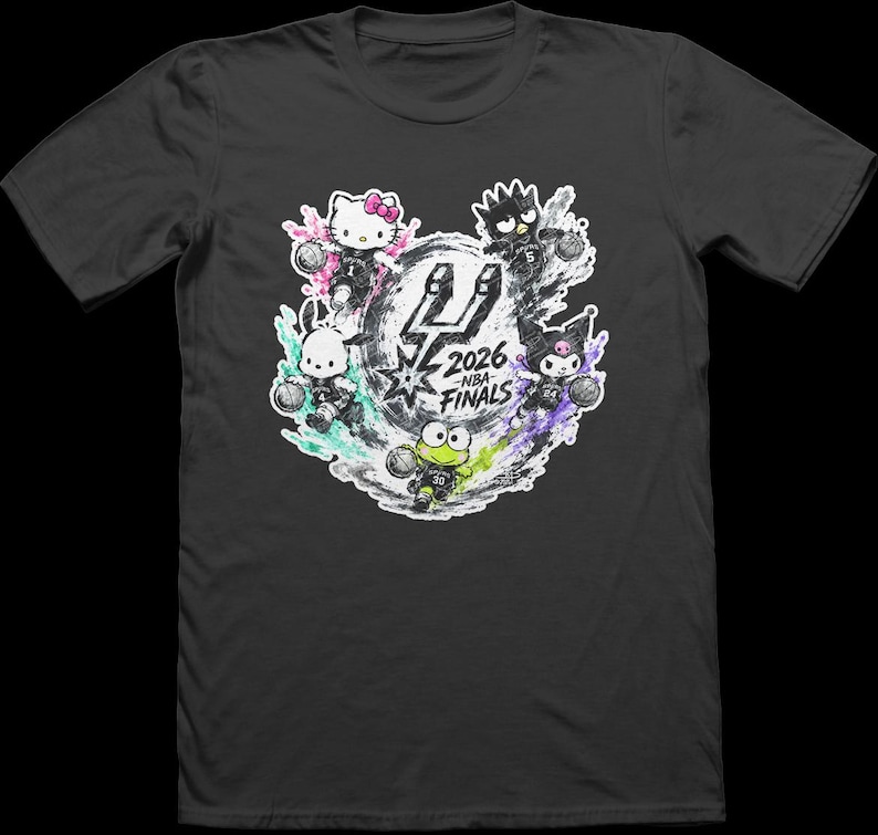 May include: A charcoal gray short-sleeve t-shirt featuring a graphic print of five Sanrio characters playing basketball. The center displays the San Antonio Spurs logo with the text 2026 NBA FINALS. Each character is surrounded by colorful paint splatters.
