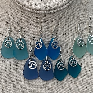 May include: A set of eight sea glass earrings with silver wave charms. The earrings are in shades of blue and green, with each pair featuring a different shade.