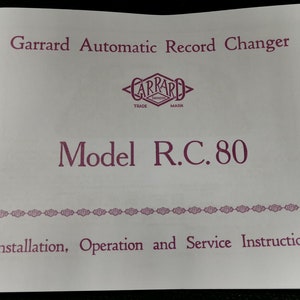 以下が含まれることがあります： Garrard 自動レコードチェンジャー、モデル R.C. 80 の白い取扱説明書。マニュアルには、ピンクのロゴに「Garrard」というテキストと、「設置、操作、およびサービスの説明」という単語が書かれています。