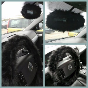 May include: Black faux fur steering wheel cover and rearview mirror cover for a car. The steering wheel cover is thick and fluffy. The rearview mirror cover is round and has a fluffy texture.