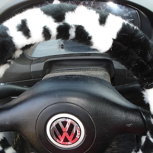 May include: Black and white faux fur steering wheel cover with a black leather steering wheel underneath. The steering wheel has a silver Volkswagen logo in the center.