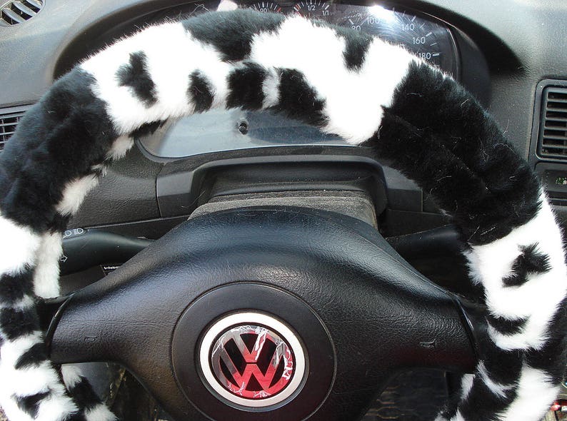 May include: Black and white faux fur steering wheel cover with a black leather steering wheel underneath. The steering wheel has a silver Volkswagen logo in the center.
