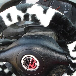 May include: Black and white faux fur steering wheel cover. The cover is made of soft, plush material and has a cowhide pattern. The cover is designed to fit most standard steering wheels.