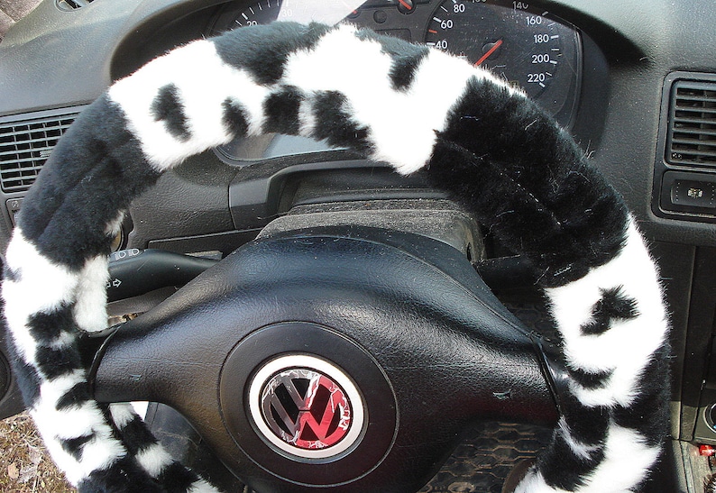 May include: Black and white faux fur steering wheel cover. The cover is made of soft, plush material and has a cowhide pattern. The cover is designed to fit most standard steering wheels.