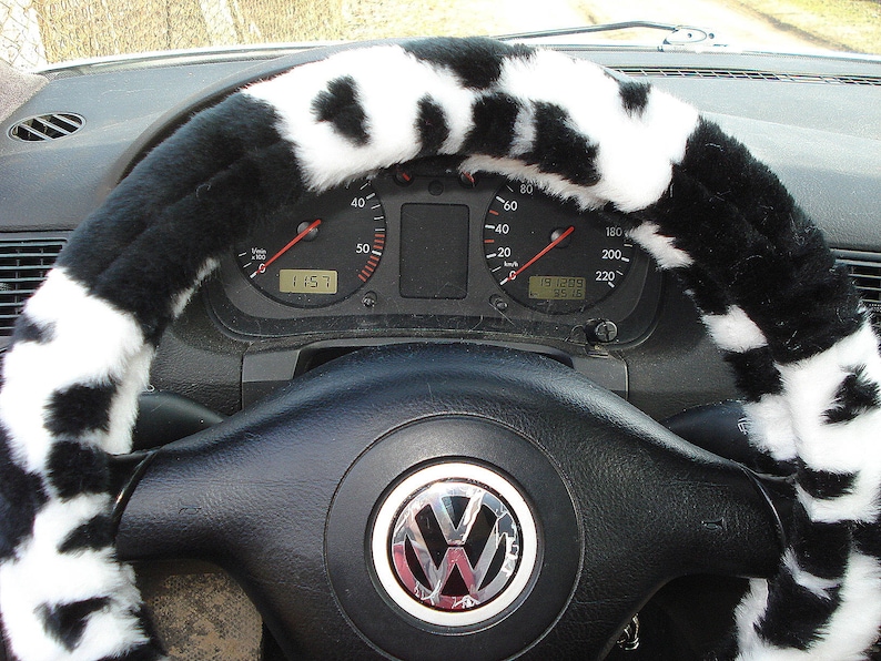 May include: A black and white cow print steering wheel cover. The cover is made of soft, plush material and is designed to fit most standard steering wheels.