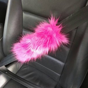 May include: A pink fuzzy car seatbelt cover. The cover is made of soft, fluffy material and is designed to add comfort and style to your car's interior.