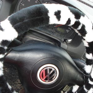 May include: Black and white cow print steering wheel cover. The cover is made of soft, plush fabric and is designed to fit most standard steering wheels.