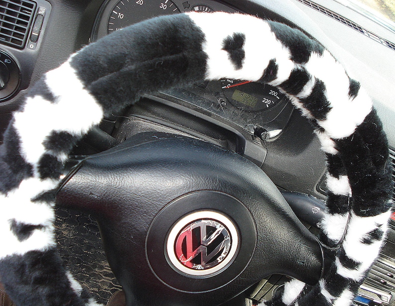 May include: Black and white cow print steering wheel cover. The cover is made of soft, plush fabric and is designed to fit most standard steering wheels.