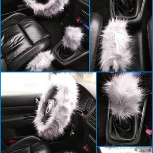May include: A set of three gray faux fur car accessories. The set includes a steering wheel cover, a gear shift cover, and a parking brake cover.