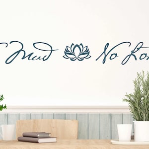 May include: A white wall with a blue and white wall decal that reads "No Mud No Lotus" with a stylized lotus flower in between the words. The decal is above a wooden table with two potted plants and a stack of books.