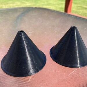May include: Two black plastic cones with a small hole at the top. The cones are sitting on a table.
