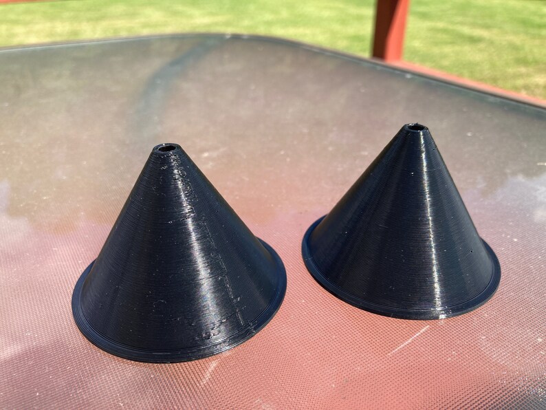 May include: Two black plastic cones with a small hole at the top. The cones are sitting on a table.