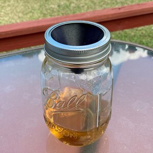 May include: A clear glass jar with a silver lid and a black lid insert. The jar is filled with a light brown liquid and the label reads "Ball Mason".