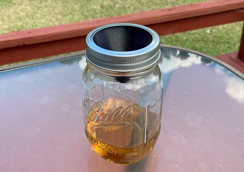 May include: A clear glass jar with a silver lid and a black lid insert. The jar is filled with a light brown liquid and the label reads "Ball Mason".