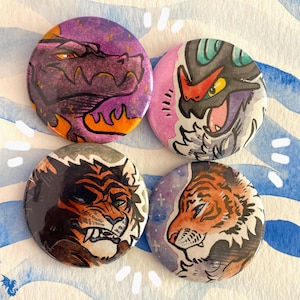 May include: Four round buttons with fantasy creature illustrations. The buttons feature a purple dragon, a black and pink creature, a lion, and a tiger. Each button has a unique design with vibrant colors and detailed artwork.