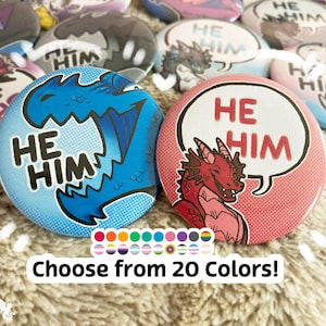 May include: Two button pins with a comic book style design. The first pin is blue with a dragon and the text "HE HIM". The second pin is pink with a red dragon and the text "HE HIM".