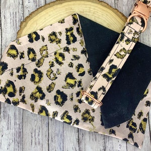 May include: A pink and black dog collar and matching bandana with a gold leopard print pattern. The collar has a rose gold buckle.