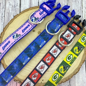May include: Four different dog collars with NFL team logos. The collars are pink with blue trim, blue with white trim, red with white trim, and green with yellow trim. The logos are for the Detroit Lions, Kansas City Chiefs, and Green Bay Packers.