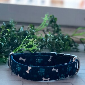 Puede incluir: Un collar para perro azul oscuro con un patr&oacute;n de huesos y huellas blancas. El collar tiene una hebilla plateada y un anillo en D plateado.