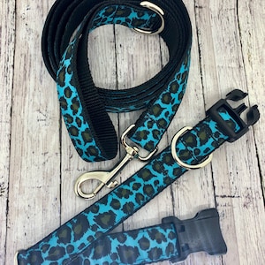 May include: A turquoise and black leopard print dog collar and leash set. The collar has a black plastic buckle and the leash has a silver hook.