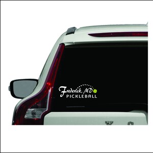 May include: White vinyl sticker on the back of a silver car with the text "Frederick, MD PICKLEBALL" and a green pickleball.