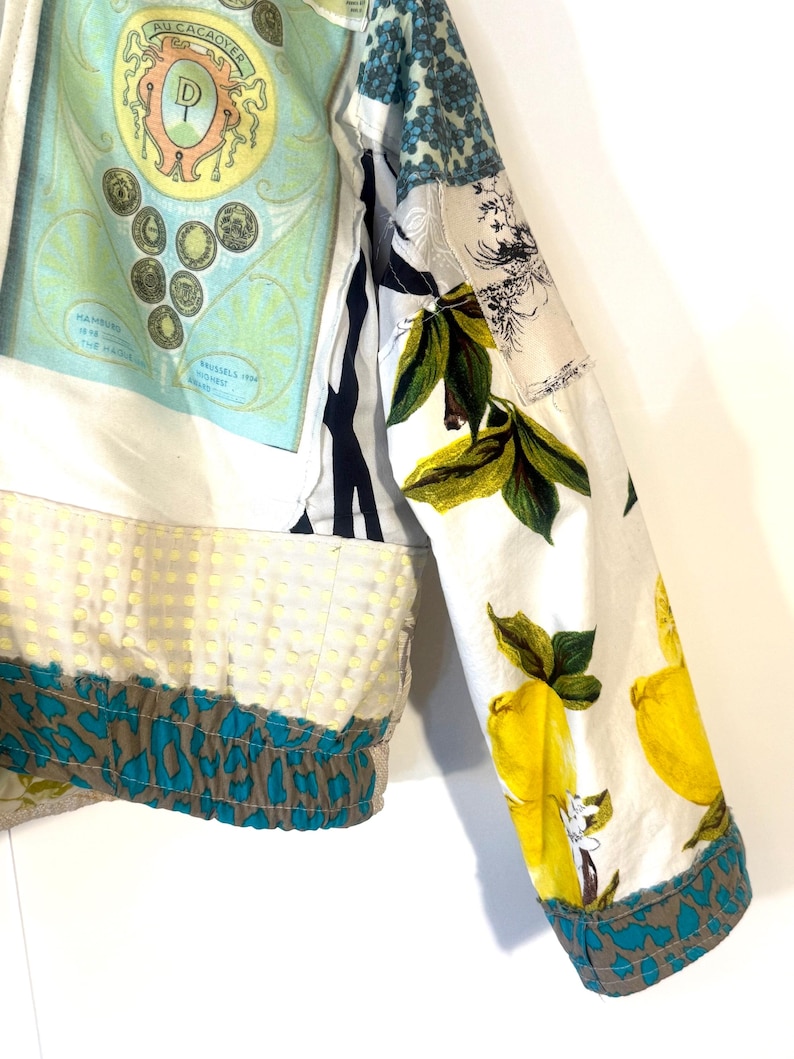 Pode incluir: Uma jaqueta patchwork com v&aacute;rios padr&otilde;es e estampas. A jaqueta apresenta uma base branca com estampas de lim&otilde;es e folhas nas mangas e uma se&ccedil;&atilde;o com um gr&aacute;fico de estilo vintage. A bainha tem uma estampa de animal em verde-azulado e marrom.