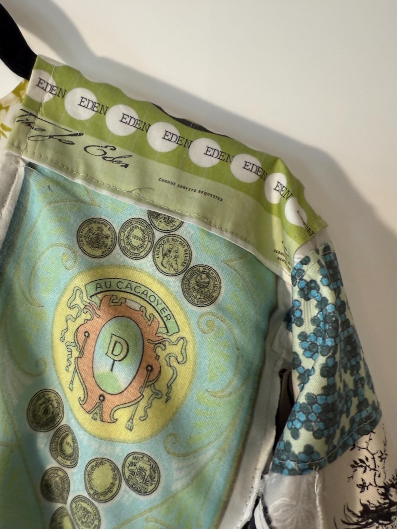 Pode incluir: Casaco com v&aacute;rios padr&otilde;es com gola verde e branca com a palavra "EDEN" num padr&atilde;o repetitivo. O forro interior apresenta um design turquesa e amarelo com ilustra&ccedil;&otilde;es de moedas e o texto "AU CACAOYER".