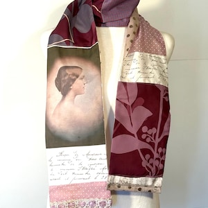 May include: A patchwork scarf with a vintage aesthetic. The scarf features a portrait, floral patterns, polka dots, and handwritten script in shades of burgundy, pink, and beige. The scarf is displayed on a mannequin.