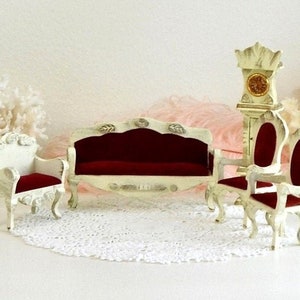 May include: A miniature dollhouse furniture set featuring a white sofa, two chairs, and a clock. The furniture is decorated with gold accents and has red velvet cushions.