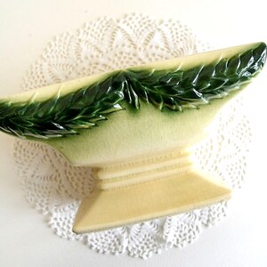 May include: A vintage ceramic planter with a green leafy design. The planter is shaped like a pedestal with a wide, shallow bowl on top. The planter is in excellent condition with no chips or cracks.